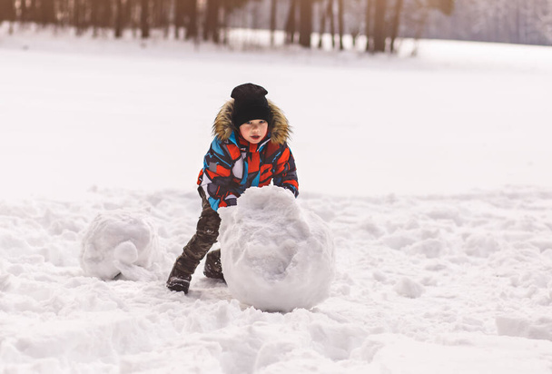 Pieni poika veistää lumipallon talvella puistossa - Valokuva, kuva