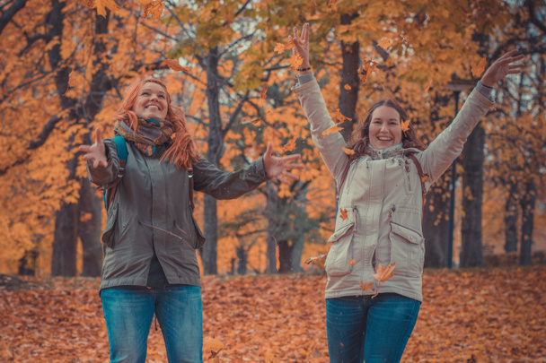Zwei Frauen werfen im romantischen Wald Herbstblätter in die Luft. Zwei Mädchen spielen im Wald mit Blättern. Romantisches Herbstfoto. - Foto, Bild