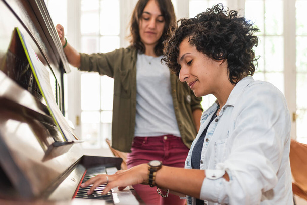 Stock photo of happy lesbian couple playing the piano in the living room at home. - Zdjęcie, obraz