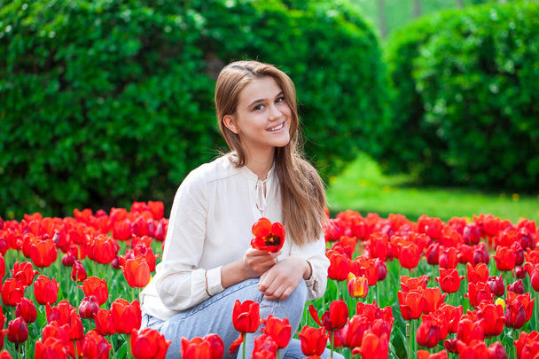 Portrait of a young beautiful girl in a summer dress posing on the lawn with red tulips - Foto, imagen