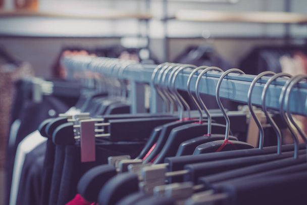 Eine Reihe unterschiedlichster Kleidungsstücke hängt in einem Textilgeschäft an einem Kleiderbügel aus klassischen Draht- und Kunststoffbügeln. Kleiderreihe in einem Geschäft. - Foto, Bild