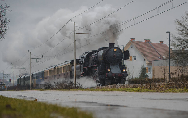 El viejo tren de vapor vintage con locomotora negra funciona a toda potencia en una vía férrea de la ciudad durante la temporada de lluvias frías. - Foto, Imagen