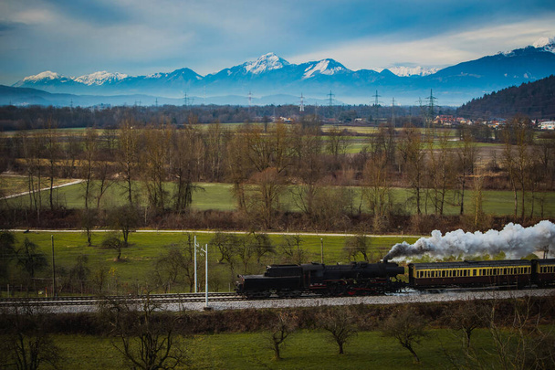 Vieux train à vapeur vintage fonctionne avec loco inversé à travers les champs avec un magnifique terrain montagneux en arrière-plan. - Photo, image