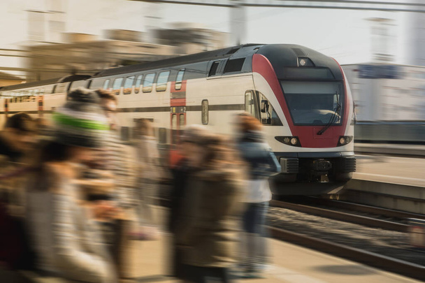 晴れた日には、スイスのローザンヌ市内の忙しい市内駅を高速通勤電車が駆け抜けています。迅速な列車を待っている通勤者. - 写真・画像