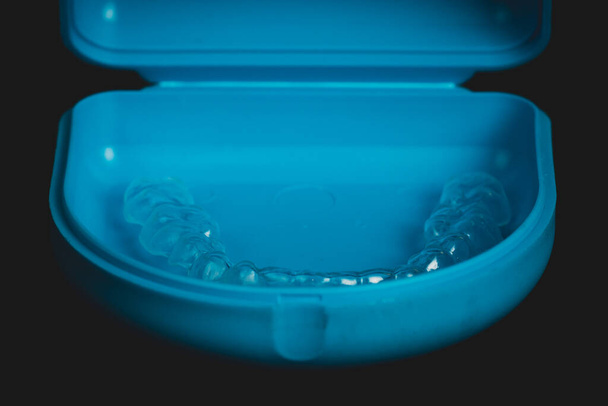 Retenção ortodôntica feita de plástico transparente em um estojo de transporte azul isolado em preto. Retentor para alinhar os dentes. - Foto, Imagem