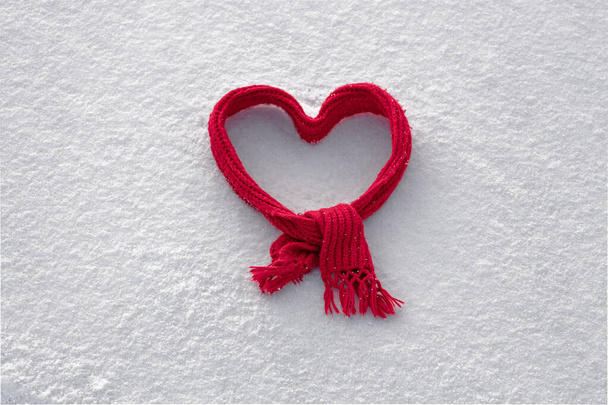 red knitted scarf folded in the shape of a heart on white snow, cute background for valentine's day - Фото, изображение