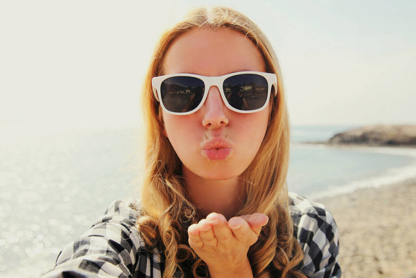 Portrait close up of happy young woman blowing her lips sending sweet air kiss stretching hand for taking selfie on a sea background - Fotoğraf, Görsel