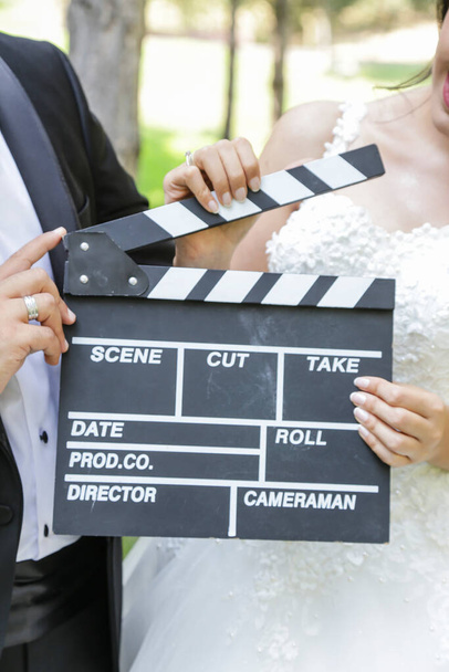 Счастливая красивая невеста и жених, женщина держит доску для клэппера, доску для кино
  - Фото, изображение
