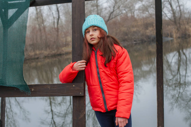 Meisje in winterkleding op een achtergrond van de rivier. Meisje van 10 jaar. Tiener in oranje jasje - Foto, afbeelding