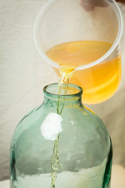 Der Prozess der Herstellung von Limoncello-Zitronenlikör zu Hause. Ein Mann gießt gefilterten Alkohol mit Zitronenschale in eine Zehn-Liter-Glasflasche. - Foto, Bild
