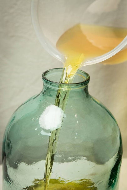 Der Prozess der Herstellung von Limoncello-Zitronenlikör zu Hause. Ein Mann gießt gefilterten Alkohol mit Zitronenschale in eine Zehn-Liter-Glasflasche. - Foto, Bild