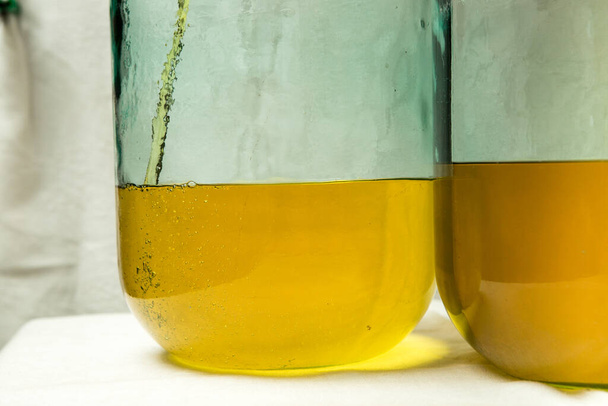 Der Prozess der Herstellung von Limoncello-Zitronenlikör zu Hause. Die Befüllung zweier Zehn-Liter-Flaschen mit dem notwendigen Alkohol, der mit Zitronenschale gefüllt ist, endet. - Foto, Bild