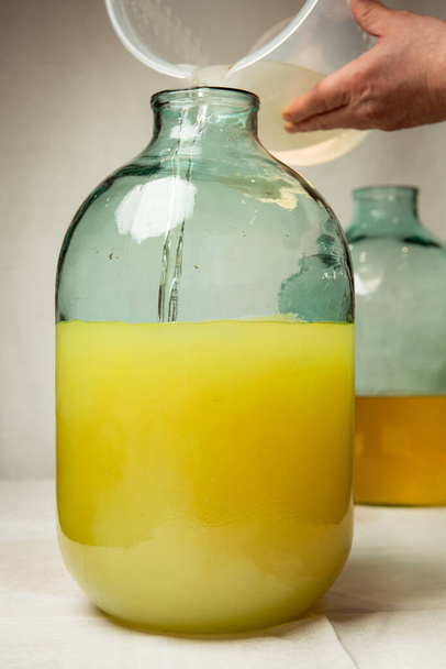 The process of making limoncello lemon liqueur at home. A man mixes lemon zest alcohol with sugar syrup in a ten-liter glass bottle. - 写真・画像