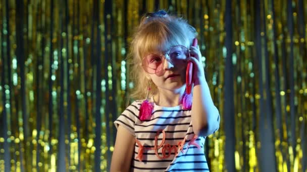Ragazza in occhiali futuristici che parla al cellulare con un amico nel night club con luce blu neon - Filmati, video