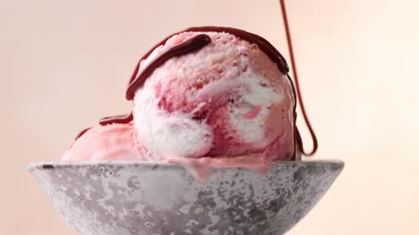 stopiony sos czekoladowy wylewa się na obracające się różowe lody deser miska zbliżenie - Materiał filmowy, wideo