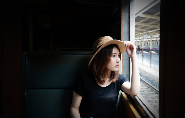 Attraktive junge Passagierin, die im Zug sitzt und durch das Fenster schaut. Teenager mit Hut fühlt sich einsam und schaut aus dem Zugfenster. - Foto, Bild