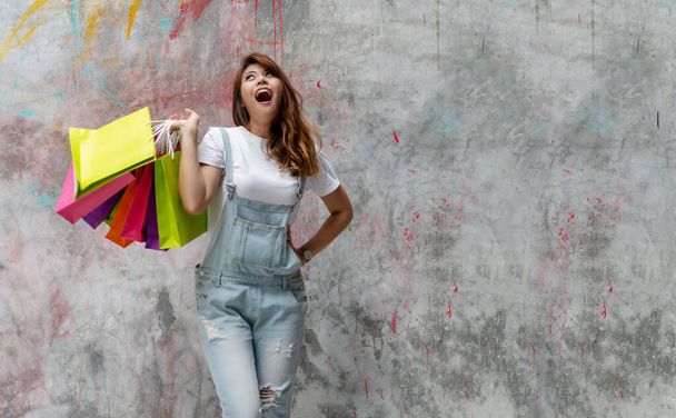 Attraktive, freudig aufgeregte junge Frau mit bunten Einkaufstüten an Betonwänden im Hintergrund mit Kopierraum. Glück, Konsumenten, Verkauf und Menschen-Konzept. - Foto, Bild