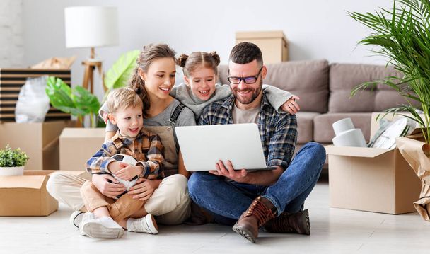 Содержание семьи, сидящей вместе на полу в новой квартире с распакованными коробками и с ноутбуком во время переезда - Фото, изображение