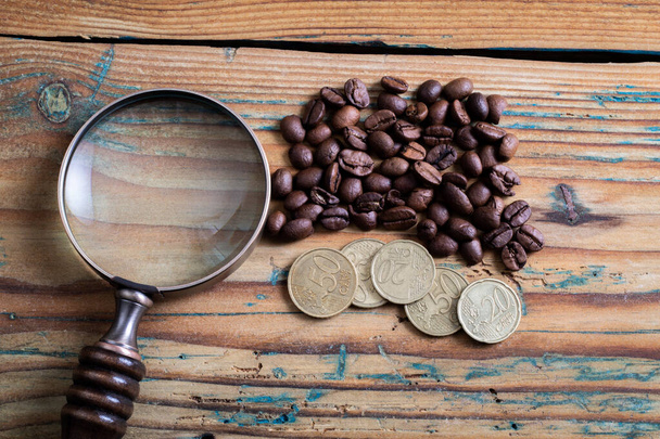 Hinnat, logistiikka ja kustannukset käsite. Eurosenttiä, kahvipapuja ja suurennuslasi puupohjalla - Valokuva, kuva