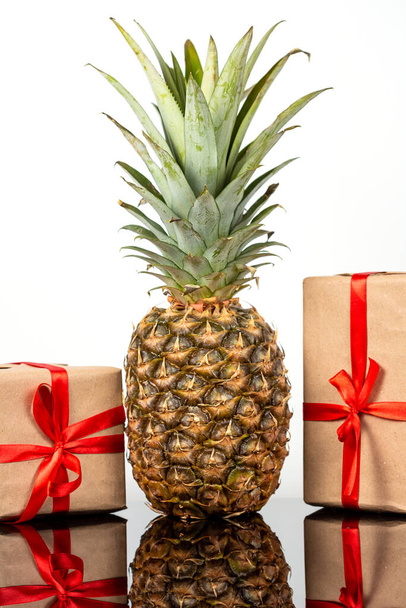 Fresh pineapple and gift boxes on black glass table on white background - Фото, изображение