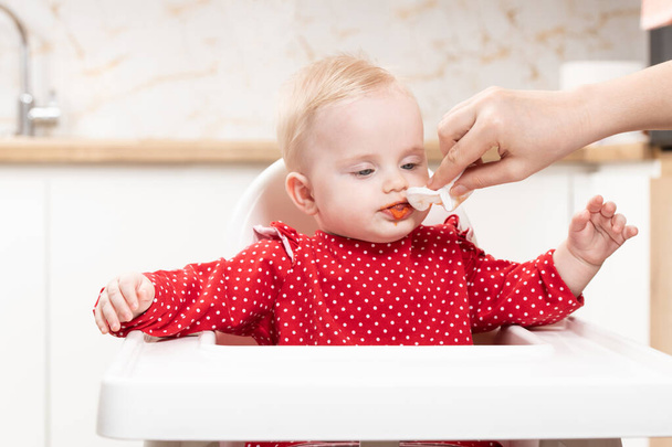 Mother Wipes Baby's Mouth With Napkin After Feeding Her Baby Daughter With Food At Home - Fotoğraf, Görsel