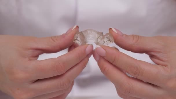 El ortodoncista muestra en sus manos un plato infantil para corregir la mordida dental. Haz una hermosa sonrisa con tecnología moderna en una clínica dental. Una sonrisa saludable en la vida es necesaria por todas las personas en el - Metraje, vídeo