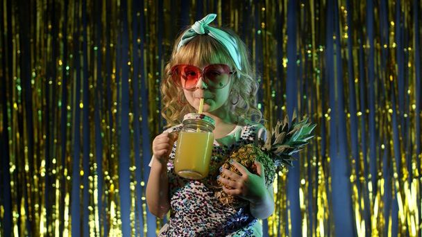 Trendy stylish child kid with pineapple fruit drinking juice in futuristic club with neon light - Photo, Image