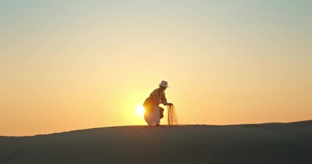 Mujer feliz con arena soplando por el viento con puesta de sol dorada en el fondo - Metraje, vídeo