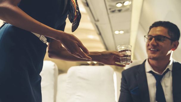 Matkustamomiehistö palvelee vettä matkustajalle lentokoneessa - Valokuva, kuva