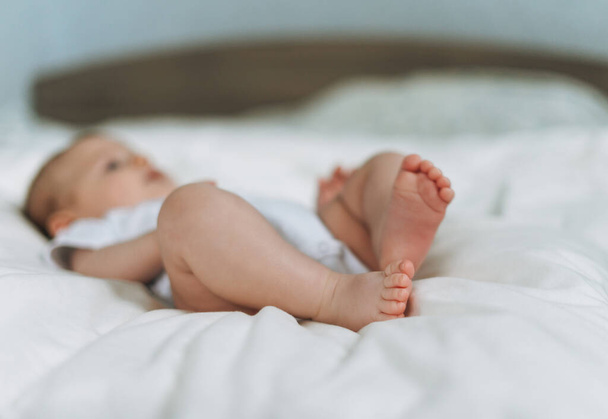 Cute baby girls 2-4 month on bed, natural tones, focus on legs - Foto, imagen