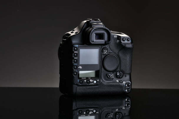 Een zwarte professionele SLR camera zit op een glazen tafel met een reflectie. Achteraanzicht. - Foto, afbeelding