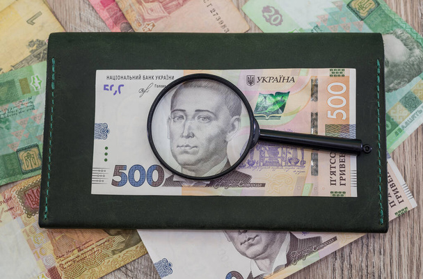 Українська гривня зі збільшувальним склом і гаманцем на фоні грошей. - Фото, зображення