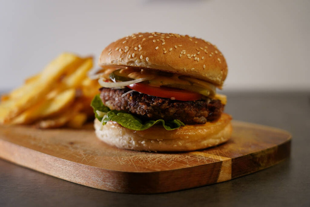 A tasty cheeseburger with French fries on a chopping board - Photo, image