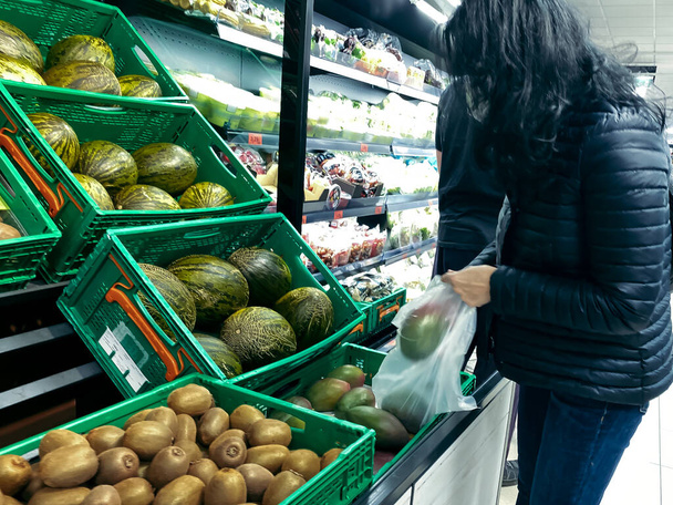Selective Focus - Woman buying mangoes in a supermarket fruit shop, protected against coronavirus wearing the KN95 face mask and gloves to pick fruit - Фото, зображення