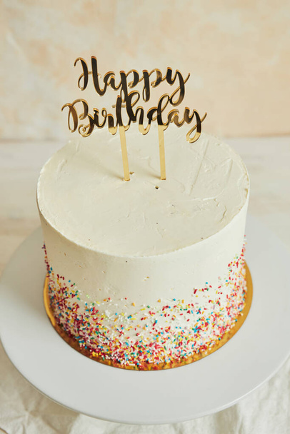 A vertical shot of a cake with a ''happy birthday'' cake topper and sprinkles on a tray - Foto, Bild