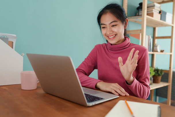 Feliz estudiante asiático saludando en línea tutor en un ordenador portátil en casa. Asia mujer Usar mangas largas rosa, Concepto de aprendizaje en línea en el hogar - Foto, Imagen
