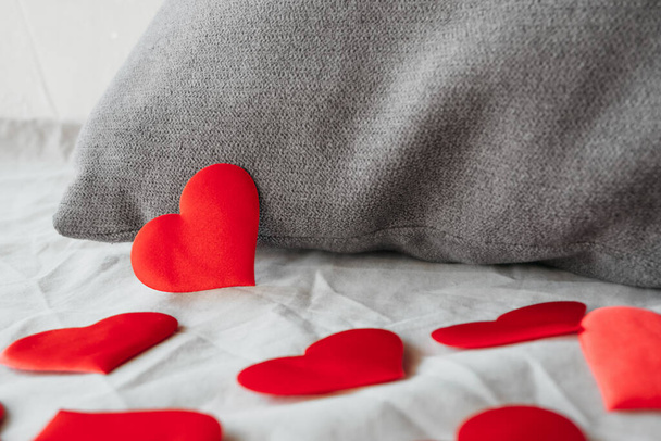 soft red hearts made of fabric near a gray pillow on beige plain bed linen, surprise for loved one on Valentines day. idea of greeting and gift. blogger content, selective focus - Photo, Image