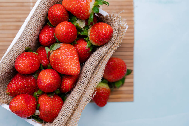 A selective focus shot of fresh strawberries on burlap and in a wooden box - Zdjęcie, obraz