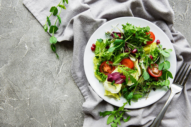Fresh green mixed  salad bowl with tomatoes and microgreens  on  concrete background. Healthy food, top view. - Photo, Image