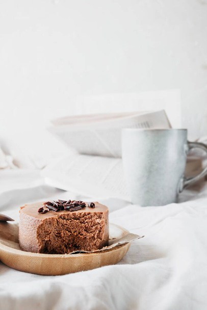 small round chocolate cheesecake without baking on reusable bamboo plate on cozy beige blanket with cup coffee and book. maintaining mental health, time spent in pleasure. vertical, selective focus - Fotó, kép
