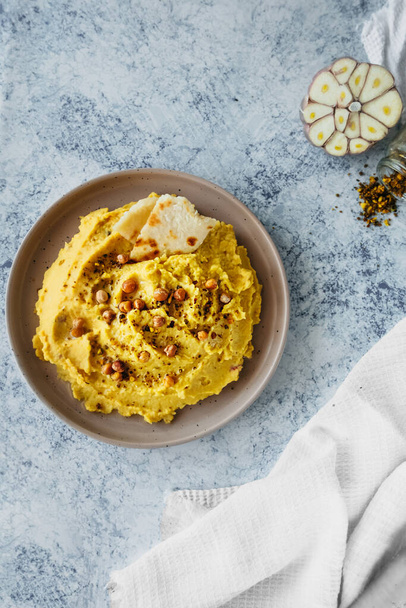 beautiful serving of chickpea hummus with olive oil, garlic, spices and roasted grains on kitchen table with cotton napkin, vertical food content, simple recipes cooking at home, selective focus - Zdjęcie, obraz