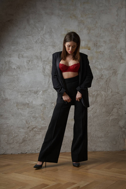 Beauty young brunette wearing black casual suit and red bra posing at apartments interior - 写真・画像