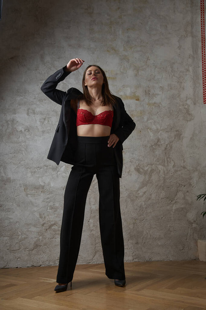 Beauty young brunette wearing black casual suit and red bra posing at apartments interior - Fotografie, Obrázek
