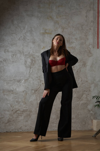 Beauty young brunette wearing black casual suit and red bra posing at apartments interior - Фото, зображення