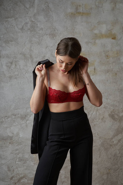 Beauty young brunette wearing black casual suit and red bra posing at apartments interior - 写真・画像