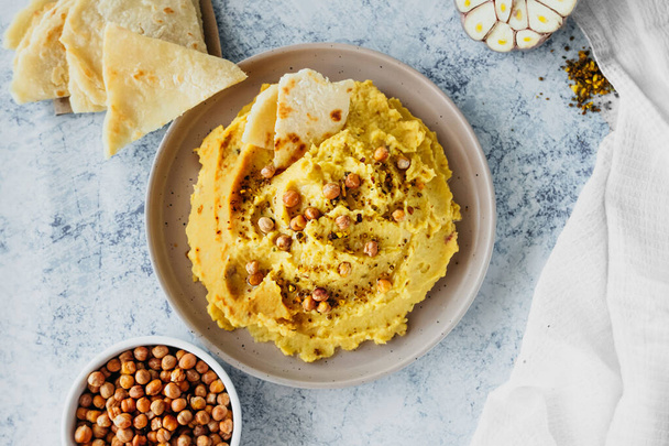 chickpea hummus with olive oil, garlic, spices and roasted grains on kitchen table with bowl of fried chickpeas and traditional tortillas, simple recipes for cooking at home, selective focus - 写真・画像