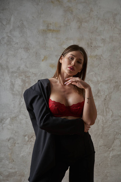 Beauty young brunette wearing black casual suit and red bra posing at apartments interior - Fotó, kép