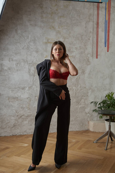 Beauty young brunette wearing black casual suit and red bra posing at apartments interior - Фото, зображення