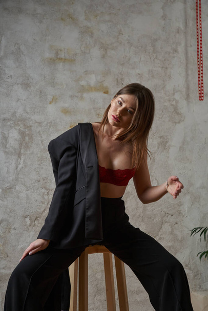 Beauty young brunette wearing black casual suit and red bra posing at apartments interior - Photo, image