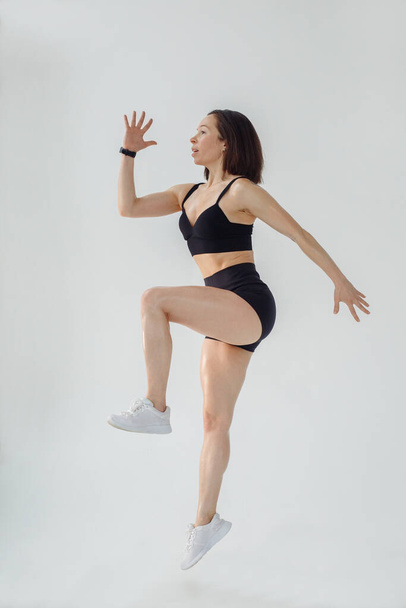 A woman in a sporty image jumps up on a white background - Foto, imagen